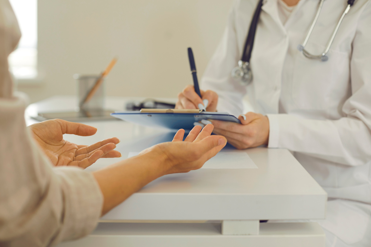 Female Doctor with Clipboard Listening to Patient and Writing down Her Health Complaints